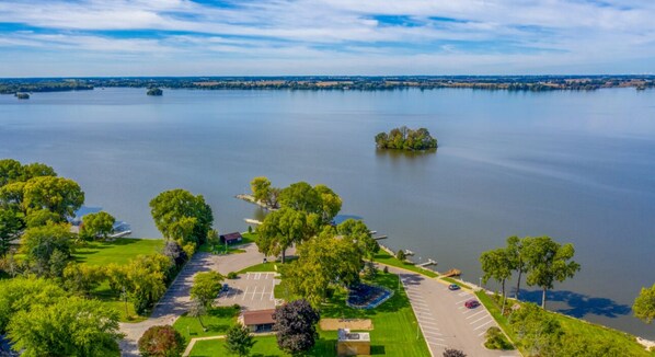 An aerial view of a lakeside property with a parking area, pathways, and a small dock.