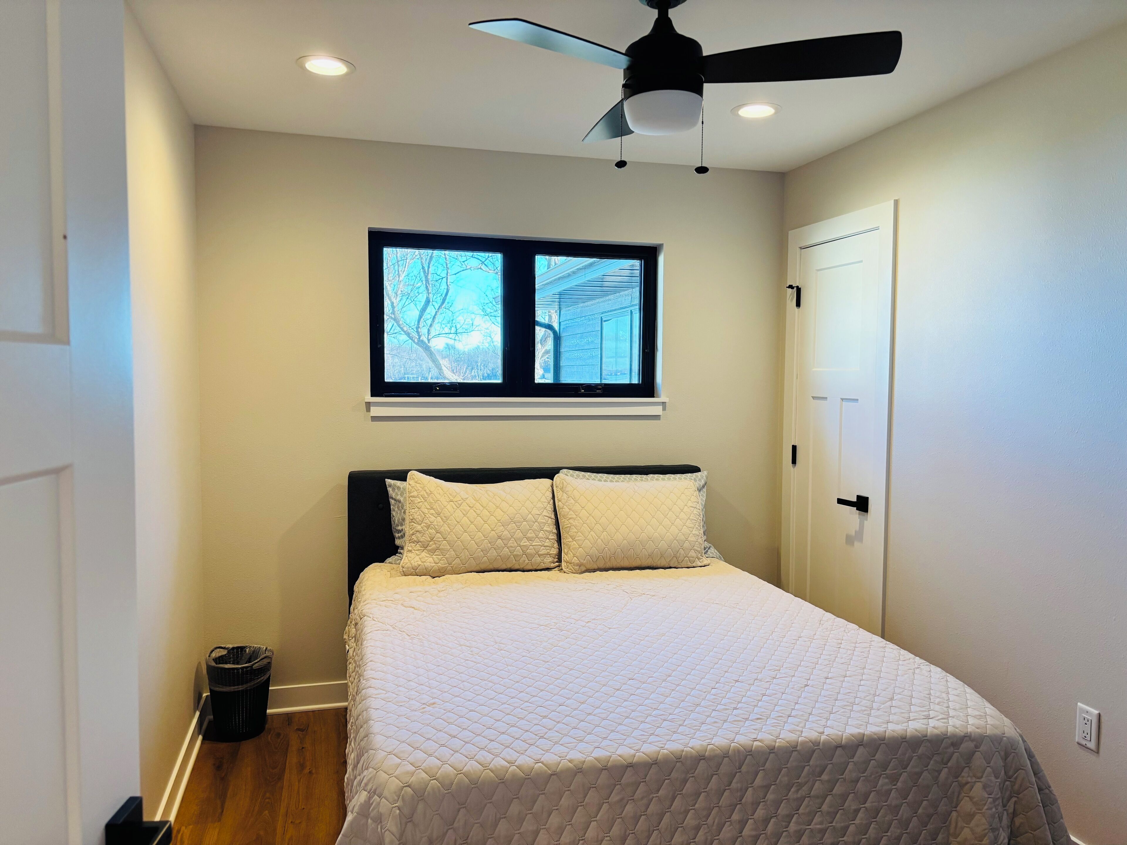A bedroom with a bed, a window, a ceiling fan, and a door.