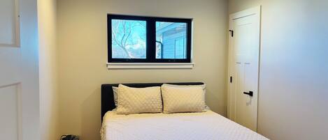 A bedroom with a bed, a window, a ceiling fan, and a door.