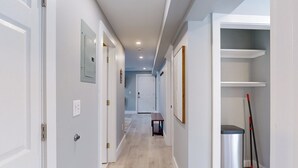 A hallway with white walls, a wooden floor, and a trash bin with a broom. - Five75 Lux PROV - Suite 3  (Providence)