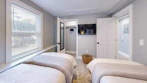A bedroom with two beds, a window with blinds, a ceiling light, and a door leading to another room. - Five75 Lux PROV - Suite 3  (Providence)
