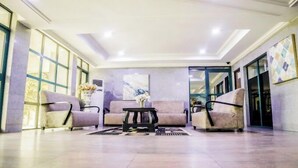 A spacious lobby with a modern design, featuring a central seating area with sofas and a coffee table, large windows on one side, and a decorative wall piece. - Muna Hotels (Jimeta)