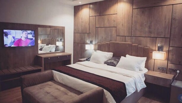 A modern hotel room with a large bed, a TV mounted on the wall, and a wooden headboard. - Muna Hotels (Jimeta)