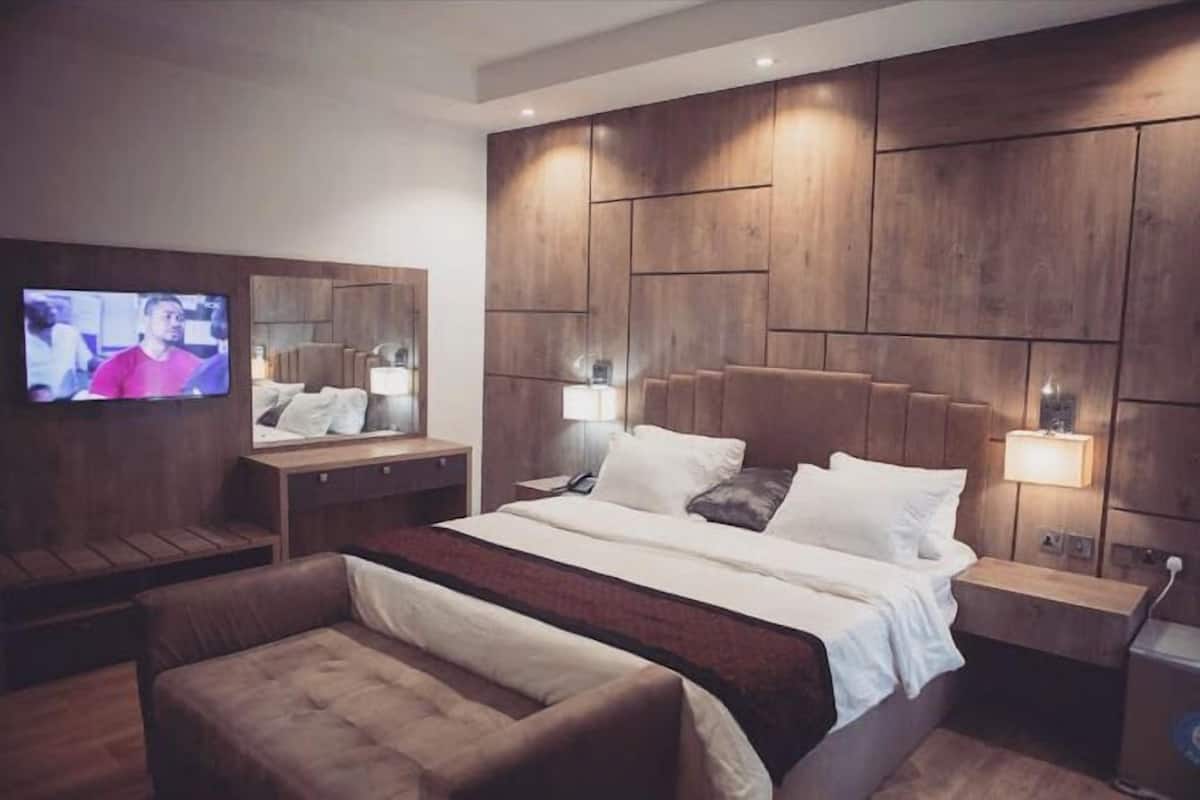 A modern hotel room with a large bed, a TV mounted on the wall, and a wooden headboard.