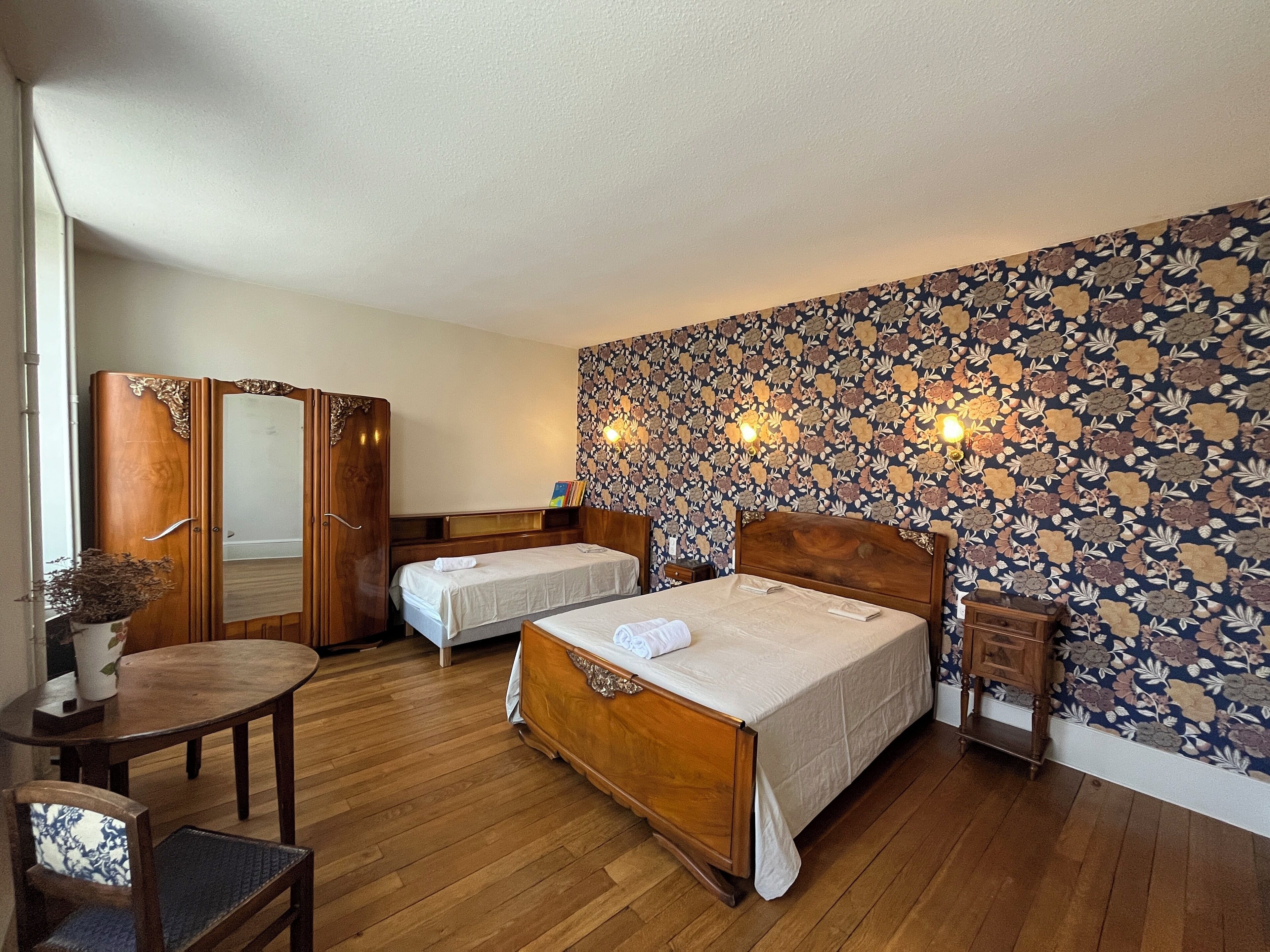 A hotel room with two single beds, a wooden wardrobe, a small table, and a chair.