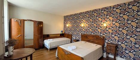 A hotel room with two single beds, a wooden wardrobe, a small table, and a chair.
