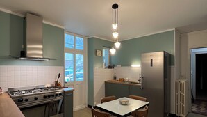 Een keuken met een gasfornuis, een koelkast, een eettafel met stoelen en een raam.
