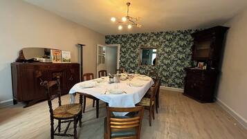 A dining room with a round table set for six, surrounded by wooden chairs. A chandelier hangs from the ceiling, and a wooden cabinet is against the wall.