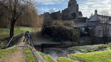 Un chemin menant à un bâtiment historique doté d’une tour, entouré de verdure et bordé d’un petit plan d’eau.