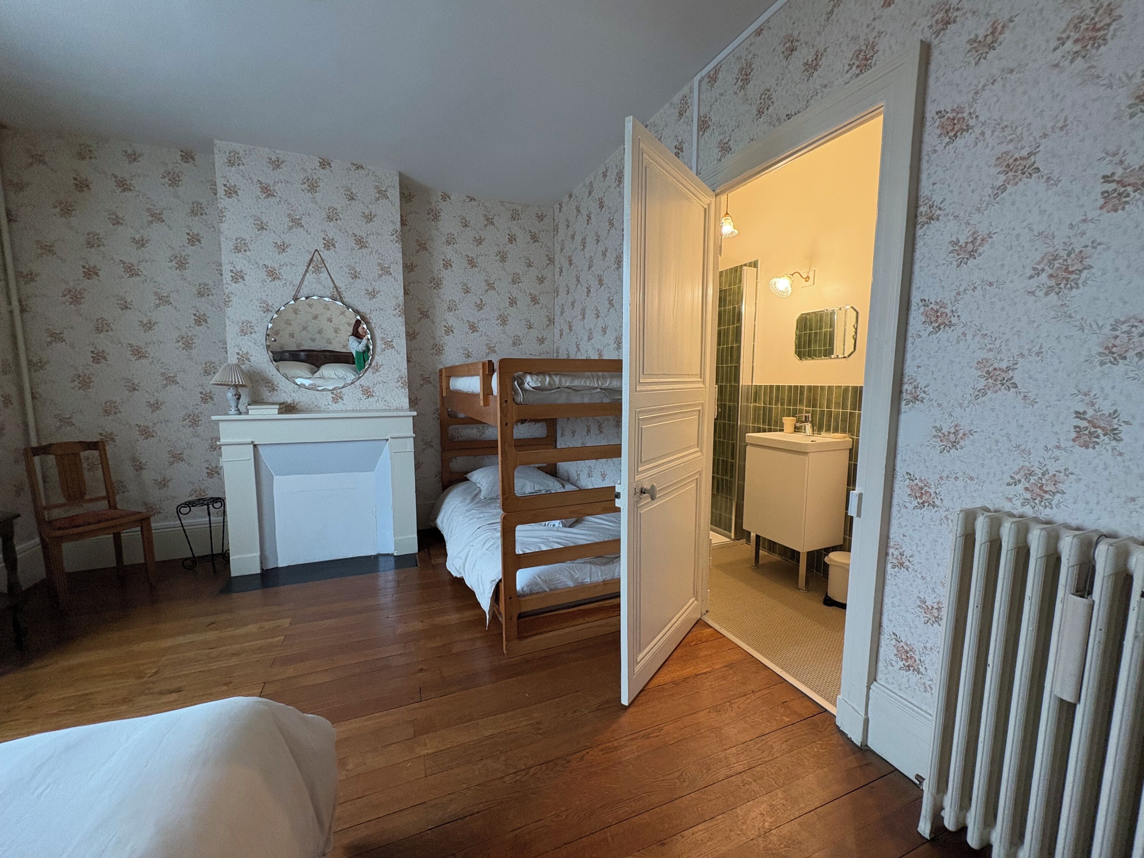 Une chambre avec un lit superposé, un petit bureau avec un miroir et une salle de bain visible à travers une porte ouverte.