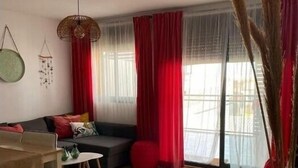 Ett modernt vardagsrum med en soffa, ett matbord och ett soffbord. Det finns röda gardiner och ett stort fönster med utsikt.