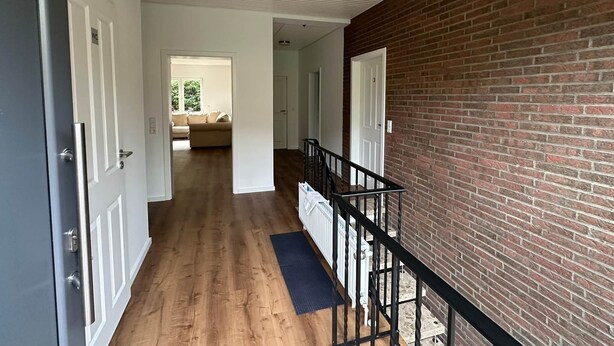 A hallway with wooden flooring, a brick wall, and a black railing. - House at the Schafwedel - Stelle (Stelle)