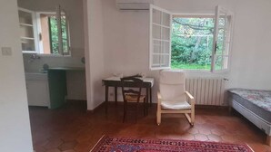 Ein Zimmer mit Bett, Stuhl, Tisch, Heizkörper und einem Fenster mit Blick ins Grüne.
