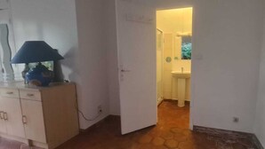 Ein Flur, der zu einem Badezimmer mit Waschbecken und Spiegel führt. Ein Schrank mit einer Lampe steht daneben.