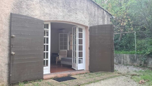 Ein rustikales Gebäude mit einer bogenförmigen Tür, die in einen kleinen Raum mit einem Bett und einem Sessel führt.