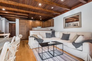 Een moderne woonkamer met een witte bank, een zwarte salontafel en houten balken in het plafond.