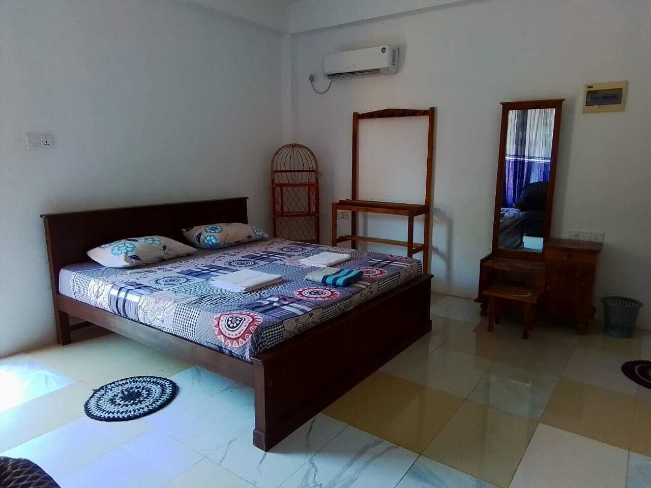 A bedroom with a bed, a wooden wardrobe, a mirror, and a small table.