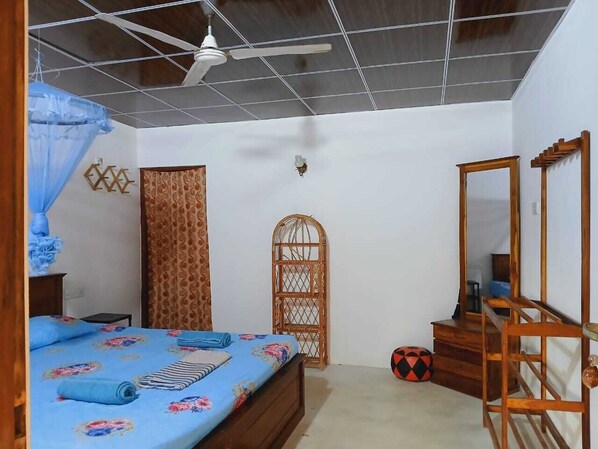A bedroom with a bed, a wooden wardrobe, a mirror, a door with a decorative pattern, and a ceiling fan.