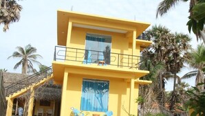 A two-story yellow building with a balcony, a staircase, and a small outdoor seating area with chairs. - Alankuda Dolphin Village (Norocholai)