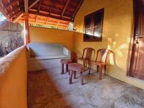 A room with a concrete floor, a bed with a wooden headboard, two small stools, and two wooden chairs. - Alankuda Dolphin Village (Norocholai)