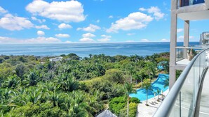 A high-rise hotel with a glass balcony overlooking a lush landscape, a swimming pool, and the ocean. - Relax in Bolongo 3BR Ocean View Condo Punta de Mita, AC and WiFi included (Corral del Risco)