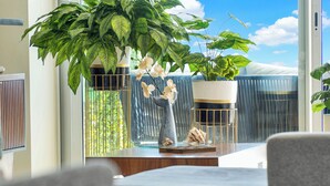 A modern living room with a large window, a potted plant, and a vase with white flowers. - Relax in Bolongo 3BR Ocean View Condo Punta de Mita, AC and WiFi included (Corral del Risco)