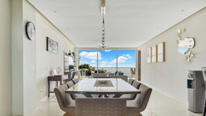 A spacious dining area with a large table and comfortable chairs, a refrigerator, and a view of the sky through large windows. - Relax in Bolongo 3BR Ocean View Condo Punta de Mita, AC and WiFi included (Corral del Risco)