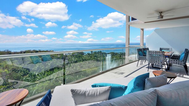 A balcony with a glass railing, outdoor furniture, and a view of the ocean and greenery. - Relax in Bolongo 3BR Ocean View Condo Punta de Mita, AC and WiFi included (Corral del Risco)