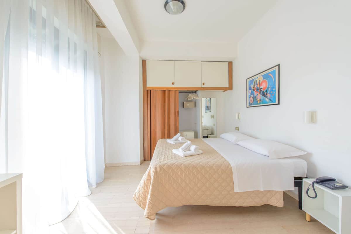 A hotel room with a bed, a bedside table, a wardrobe, and a painting on the wall.