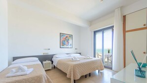 Ένα δωμάτιο ξενοδοχείου με δύο κρεβάτια, ένα τραπέζι από γυαλί, έναν πίνακα στον τοίχο και θέα στην παραλία από το παράθυρο.