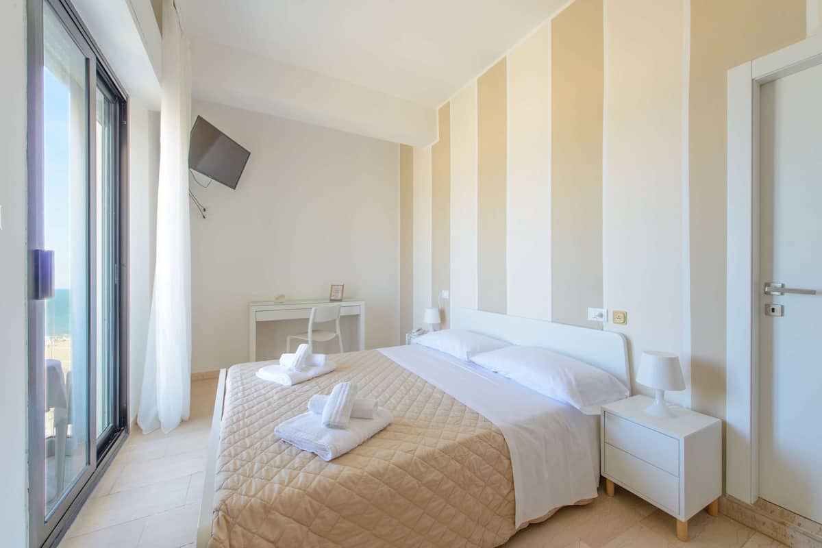 A hotel room with a bed, bedside tables, a desk, and a TV mounted on the wall.