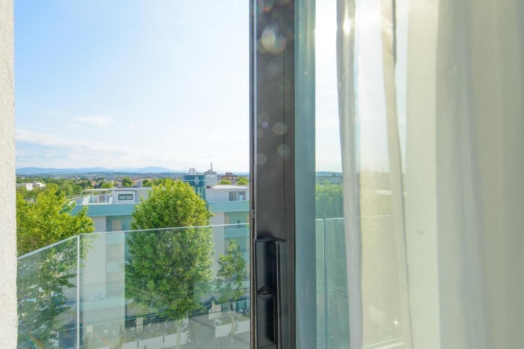 Vista da un balcone con ringhiera in vetro su una zona residenziale con case e alberi.