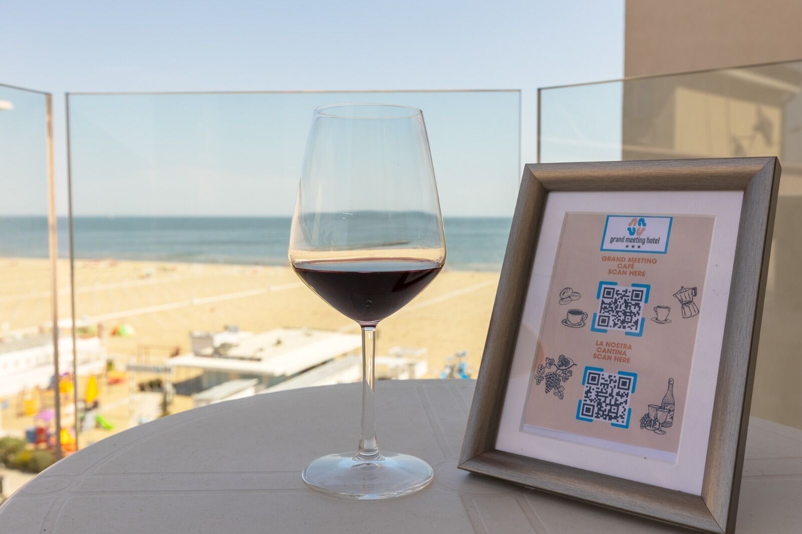 Ein gerahmter QR-Code auf einem Tisch mit einem Glas Rotwein, mit Blick auf einen Strand.