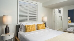 A hotel room with a large bed, two bedside lamps, a window with blinds, a door leading to another room, and a small table with a lamp. - Central, Arcade table, 5 mins to Downtown Denver (Denver)