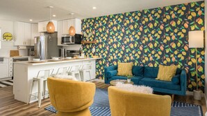A modern kitchen with white cabinets, a central island, and a microwave. There is a blue sofa with yellow cushions and a patterned wall in the living area. - Central, Arcade table, 5 mins to Downtown Denver (Denver)