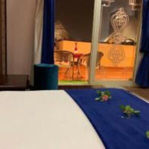 A hotel room with a bed, a blue bed runner, and a view of the outdoor area through a glass door. - Sunrise Pyramids Inn (Giza)
