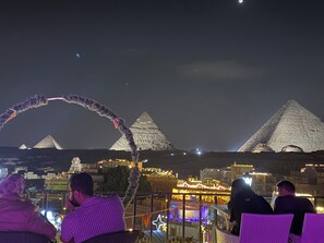 A nighttime view of the pyramids with a decorative arch and illuminated buildings in the foreground. - Sunrise Pyramids Inn (Giza)