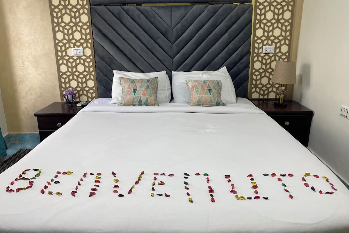 A hotel room with a large bed, two pillows, a nightstand, a lamp, and a decorative wall panel.