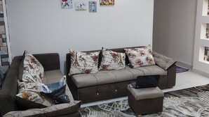 Ett vardagsrum med en soffa, fåtöljer och ett soffbord. Det finns dekorationer på väggarna och en matta på golvet.