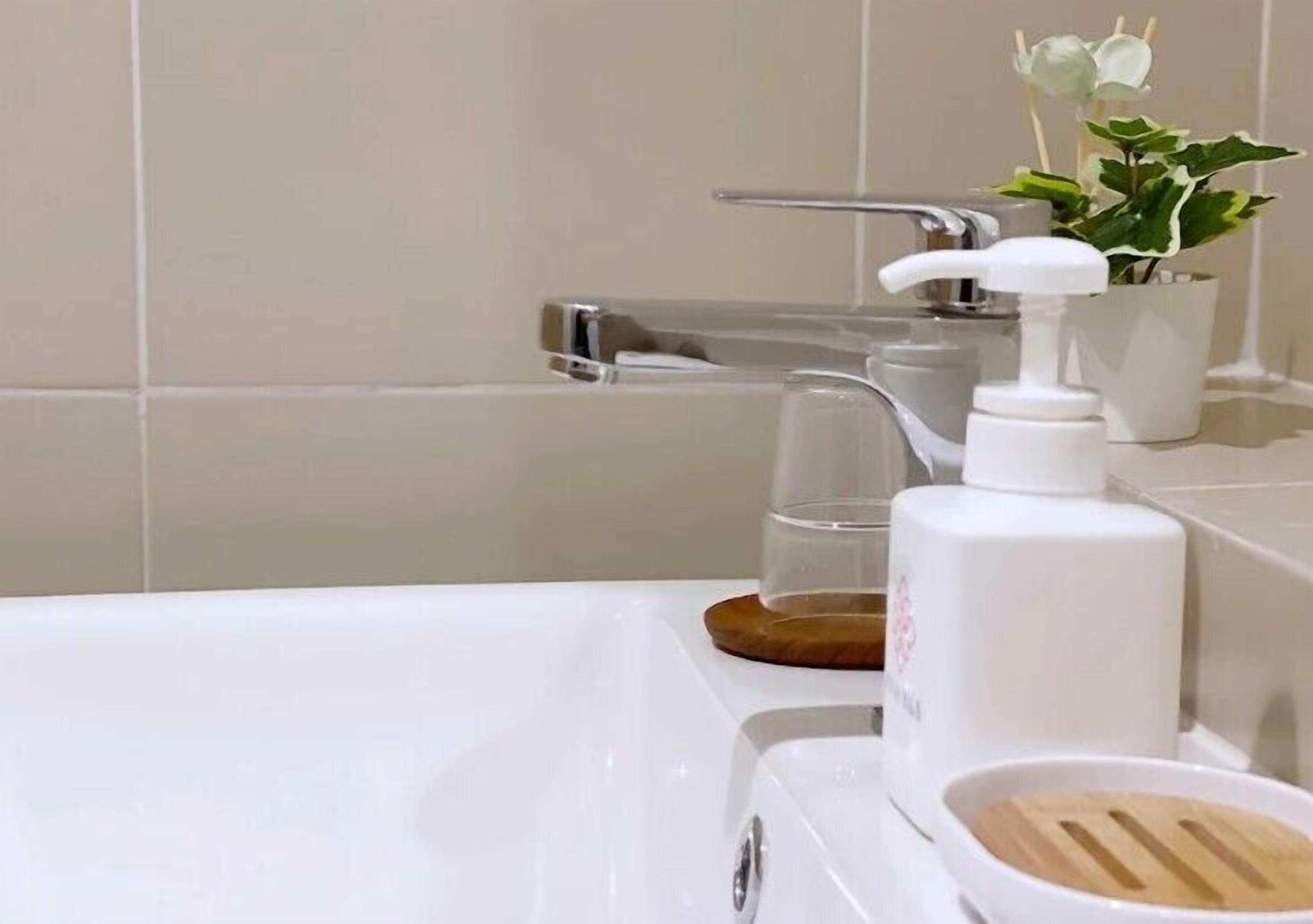 Une salle de bain avec une baignoire blanche, un verre d’eau, un distributeur de savon et une plante en pot.