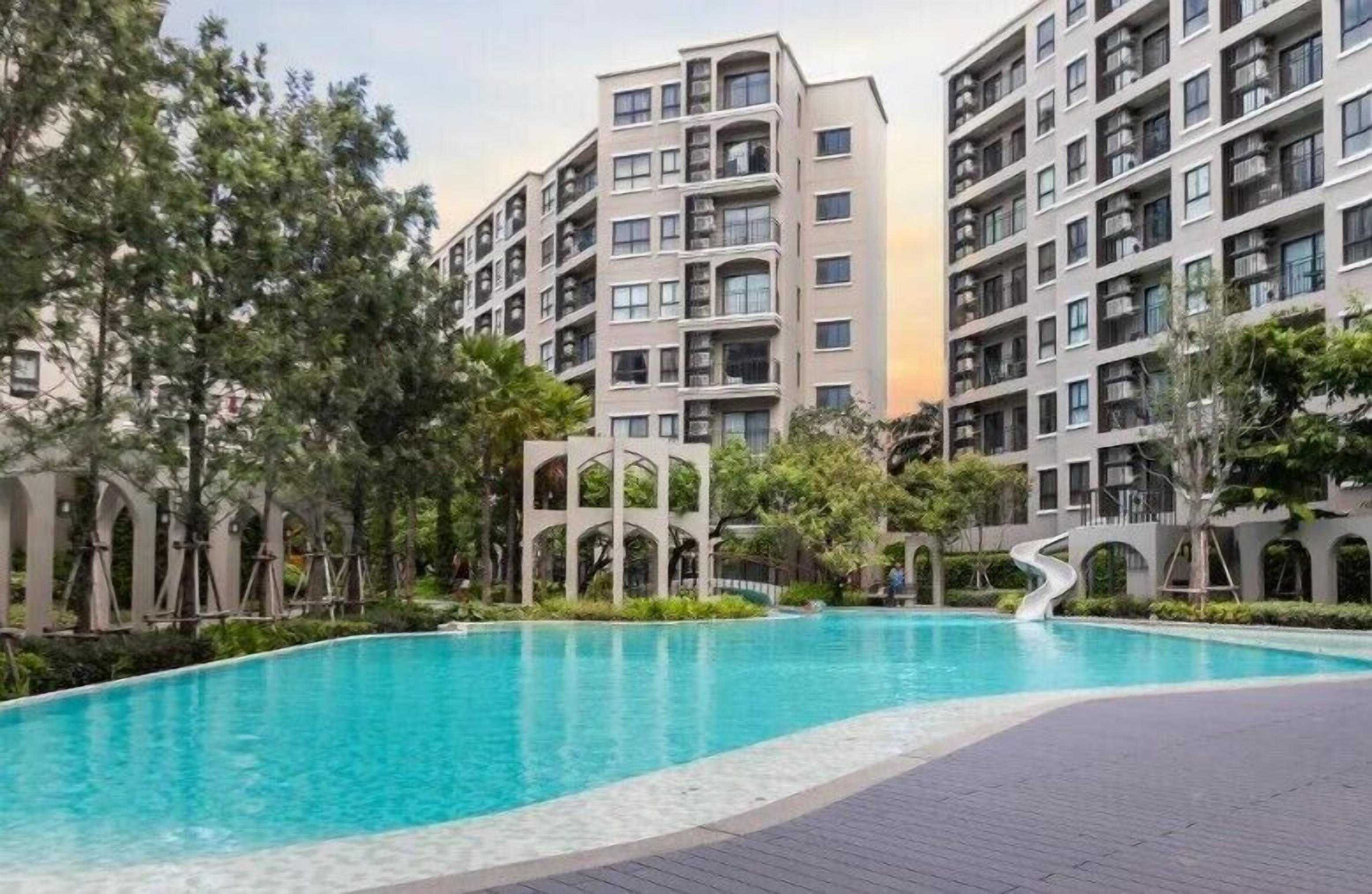 A modern apartment building with a swimming pool surrounded by greenery.