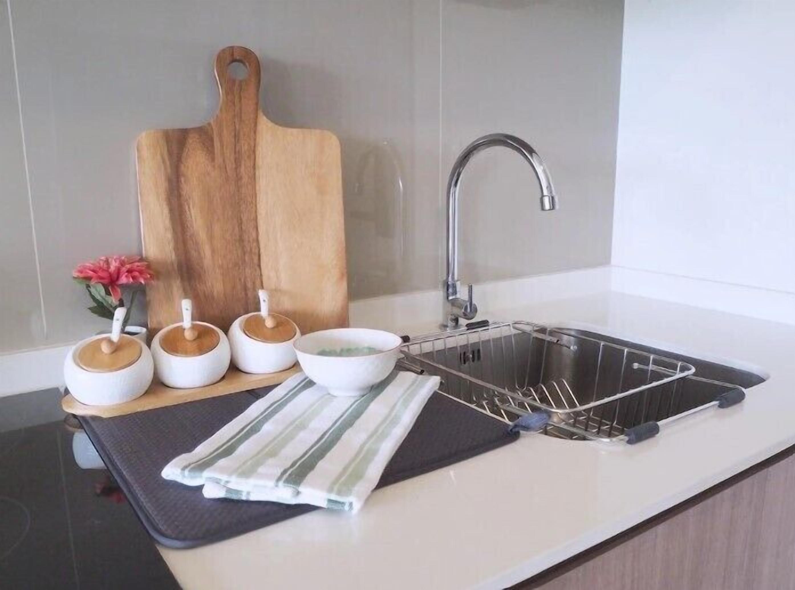 A kitchen with a stainless steel sink, a wooden cutting board, and three white ceramic containers with lids.