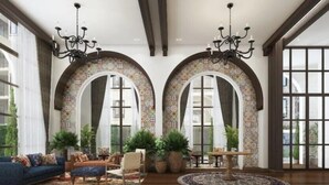 A spacious lobby with two large arched windows, a blue sofa, a round table, and several potted plants. - La Casita Hua Hin (Hua Hin)