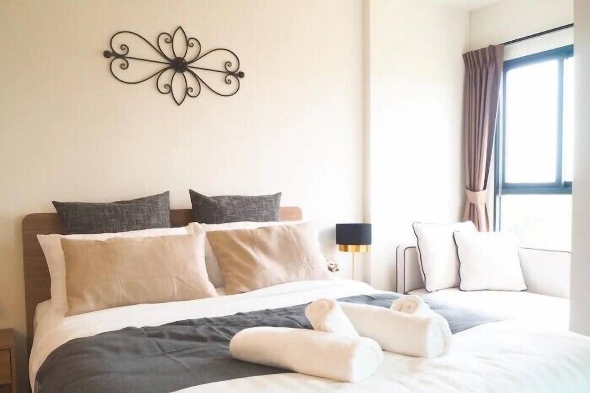 Un letto rifatto con una coperta bicolore, due cuscini e asciugamani arrotolati.
