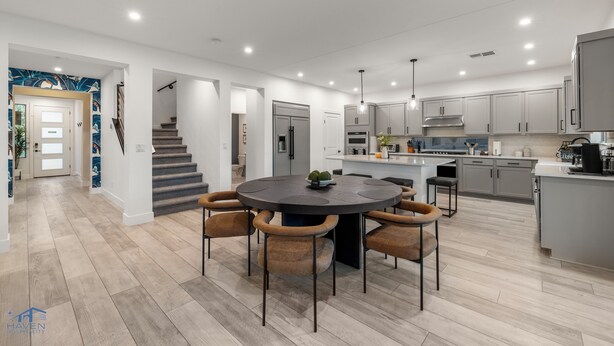 A modern kitchen with grey cabinets, a central island, and a dining area with a round table and chairs. - Cozy Modern 5bd Home, 10mins to Airport, 15mins to the Strip, Pool & Jacuzzi! (Las Vegas)