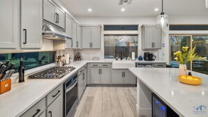 A modern kitchen with grey cabinets, a stainless steel range, and a large island with a bowl of lemons. - Cozy Modern 5bd Home, 10mins to Airport, 15mins to the Strip, Pool & Jacuzzi! (Las Vegas)