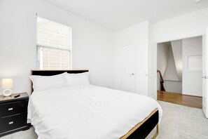 A bedroom with a bed, a nightstand, a lamp, and a window with blinds. - Lux Galleria Home-5BR Roof Deck (Houston)