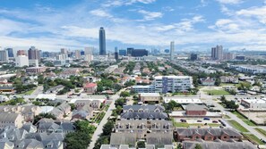 A residential area with a mix of single-family homes and apartment buildings, a central road, and a distant city skyline with high-rise buildings. - Lux Galleria Home-5BR Roof Deck (Houston)