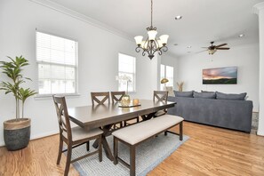 A dining area with a wooden table, chairs, and a bench. There is a chandelier, ceiling fan, and a television on the wall. - Lux Galleria Home-5BR Roof Deck (Houston)