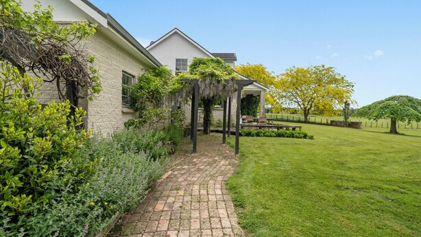 Un sendero de ladrillo que lleva a una casa con jardín y una pérgola.
